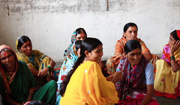 group of people with orange and yellow sari sitting around in the corner of a room