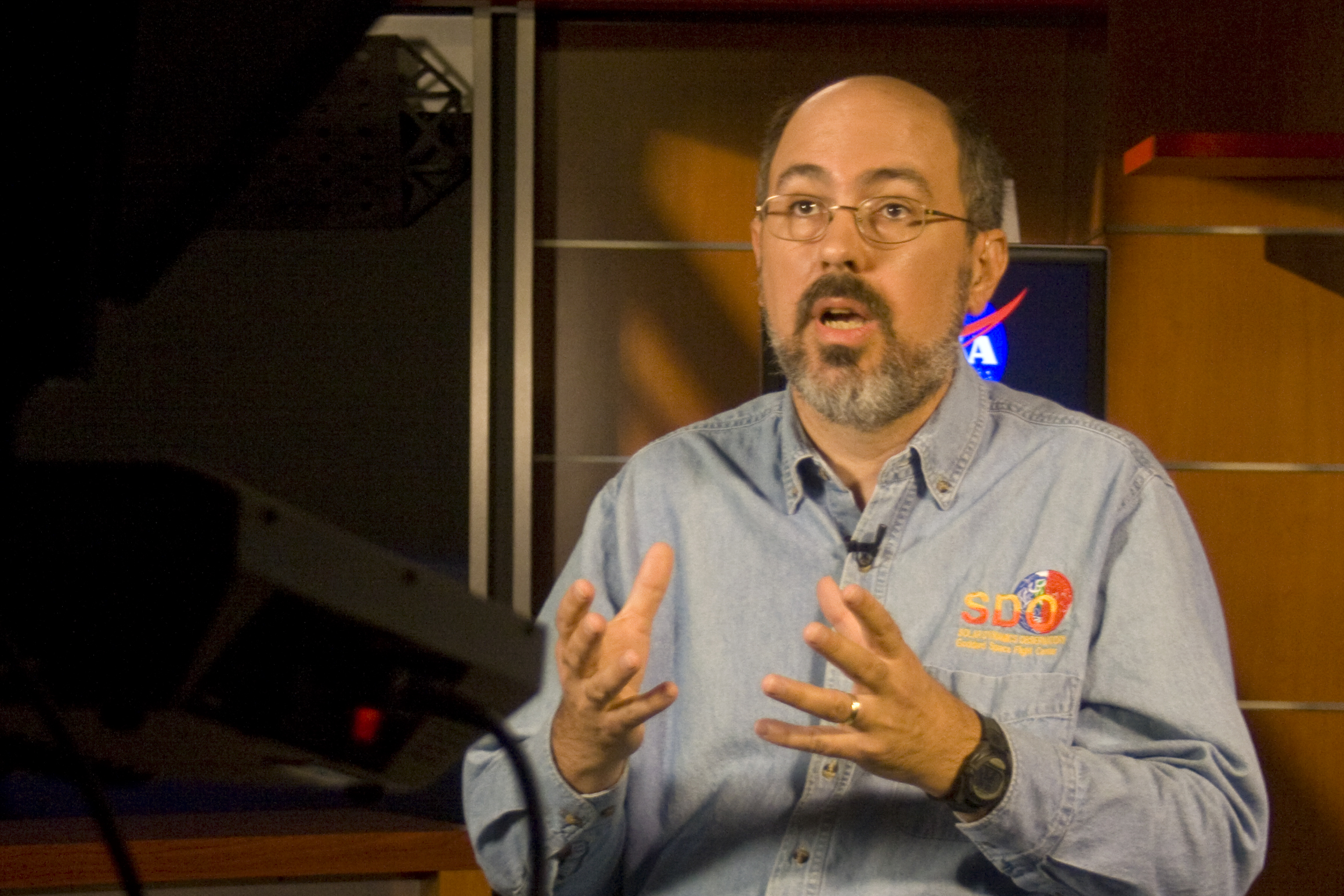 a man speaking at a television set in a room