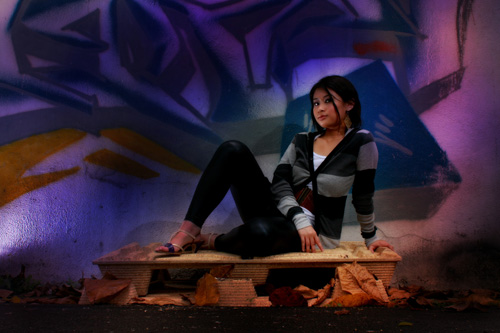 a young woman is sitting on a bench by a graffiti wall