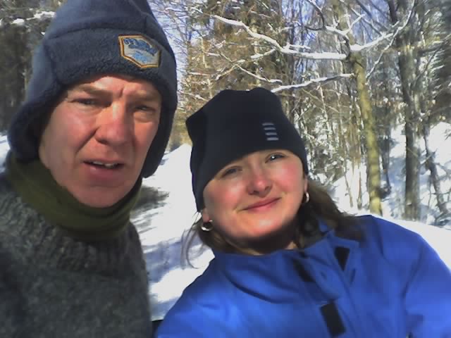 a man and a woman smile at the camera on a snowy forest path