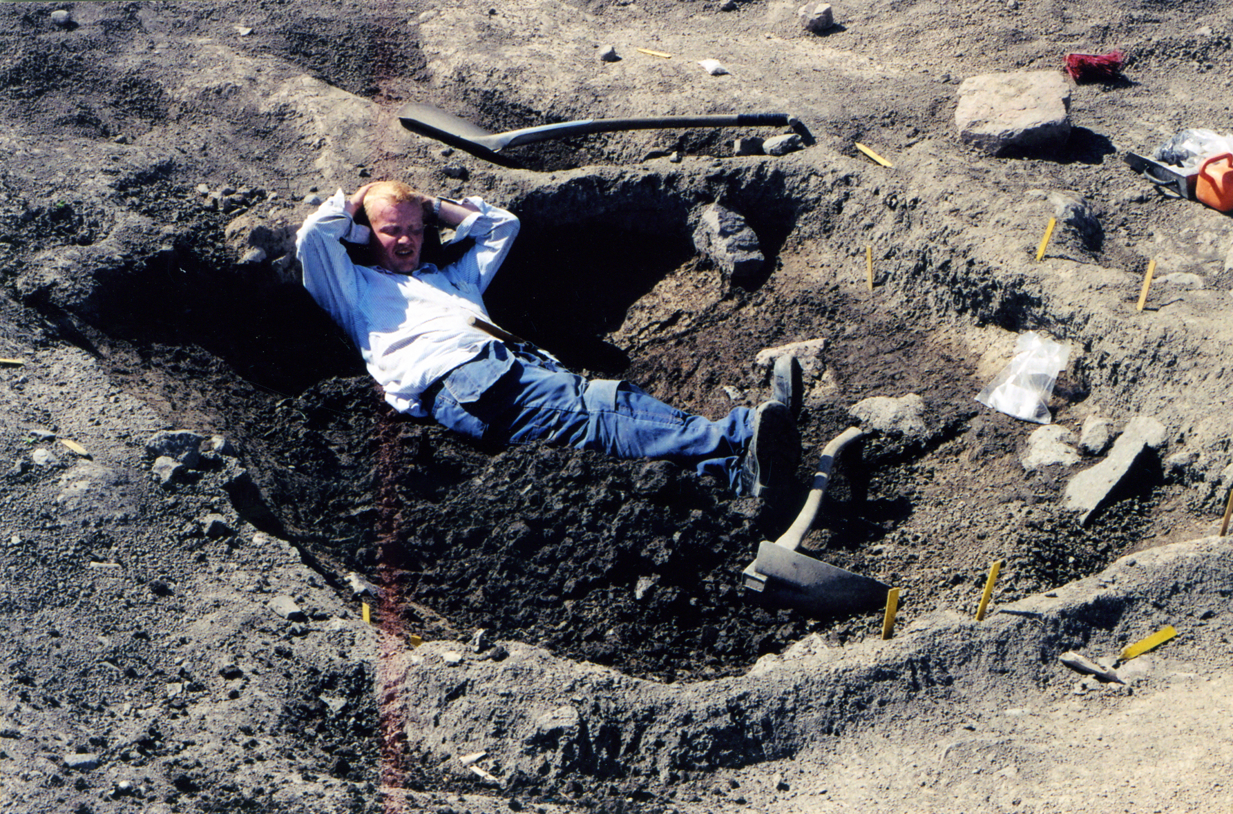 a man lying in the dirt in a hole on a cell phone