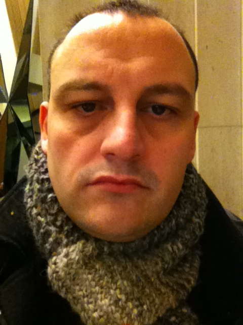 a bald man in a scarf taking a selfie