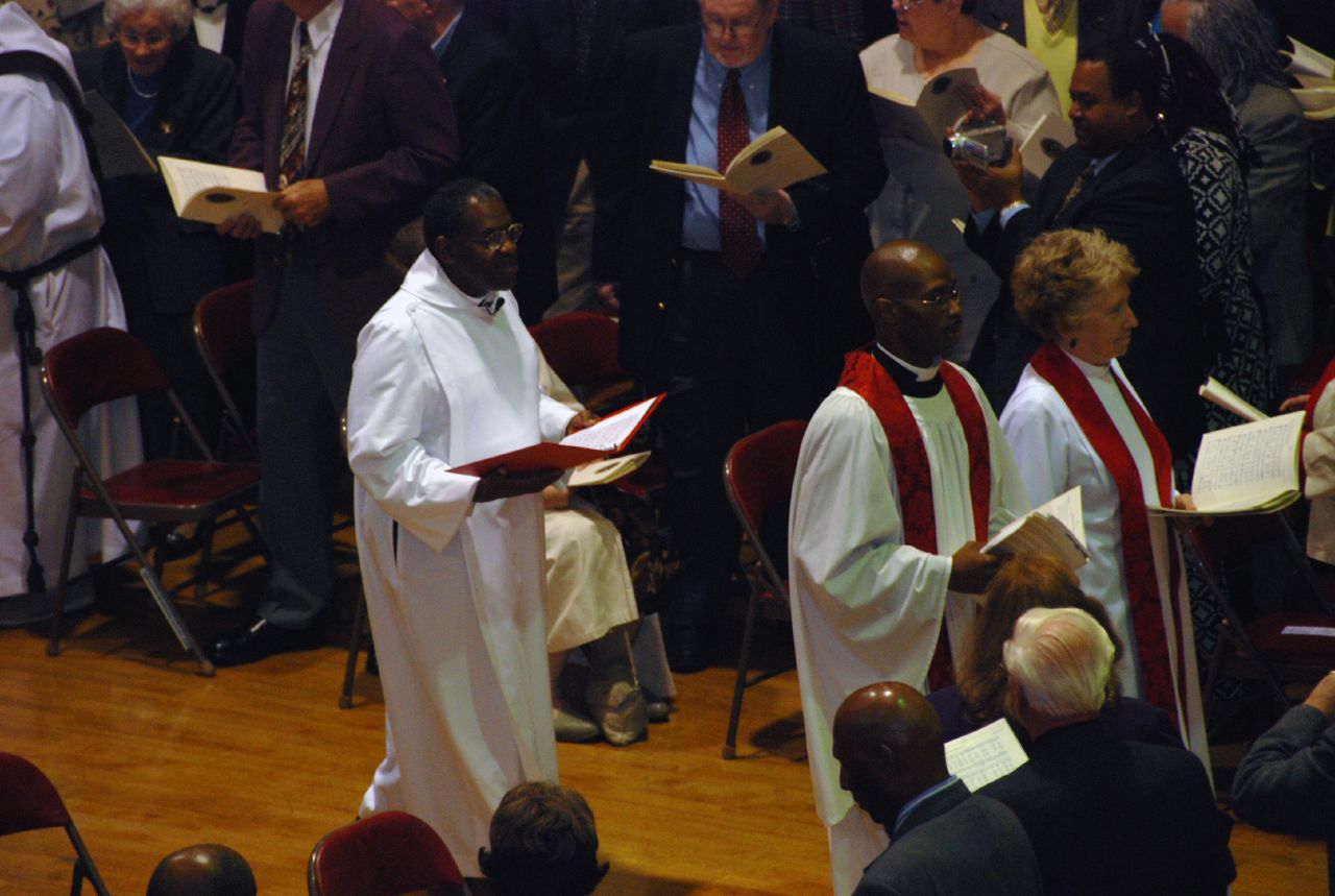 a man in clergy robes and others standing around with one person holding a large book