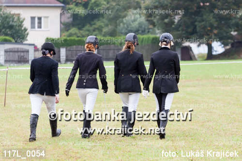 four equestrians dressed in black walking on grass