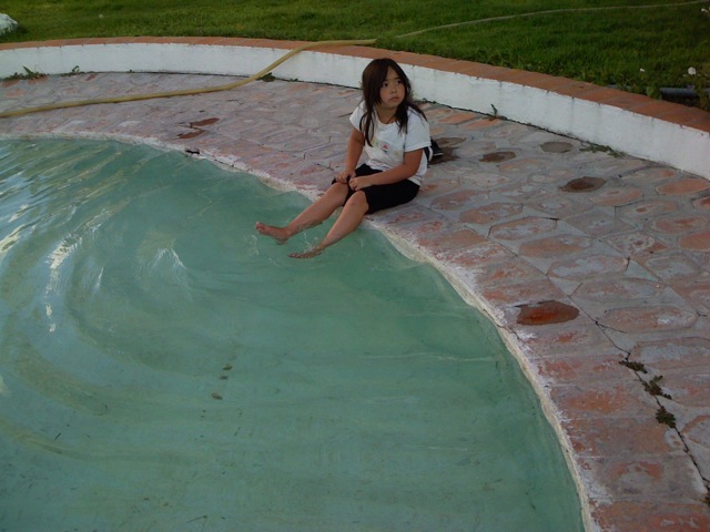 girl sitting on edge of pool looking at camera