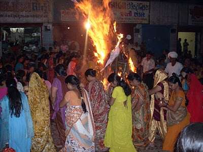 several people with saris standing around an outdoor fire pit