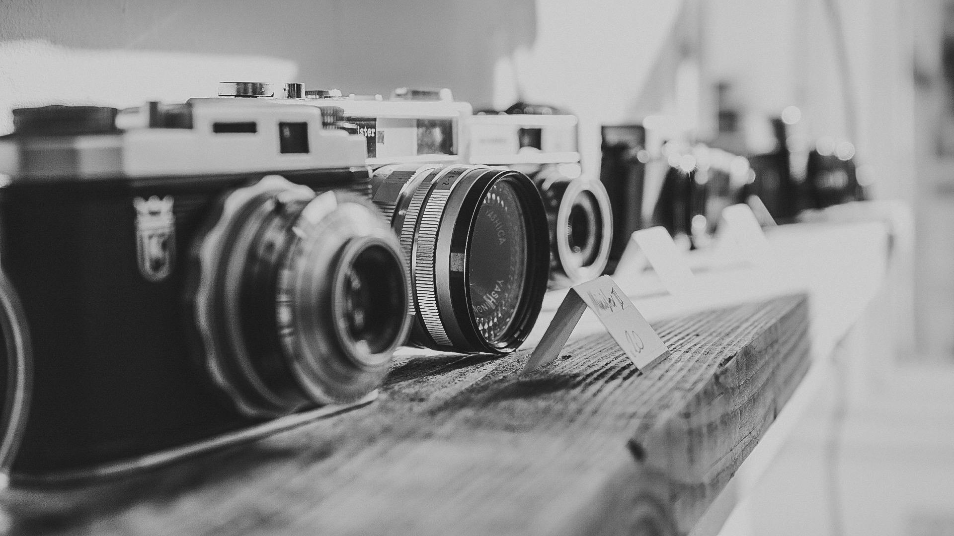 a row of cameras sitting on top of a wooden table, a black and white photo, by Adam Marczyński, pexels contest winner, in retro colors, cinematic. by leng jun, rolleiflex, cute photo