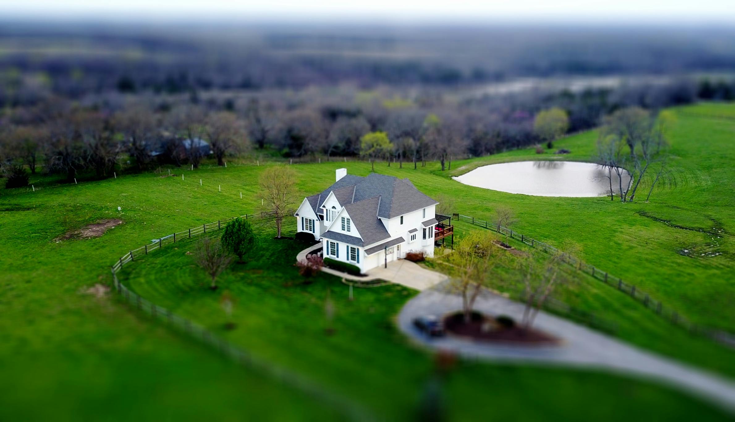 a large white house sitting on top of a lush green field, a tilt shift photo, pexels contest winner, photorealism, lake house, midwest town, drone photograpghy, model miniature