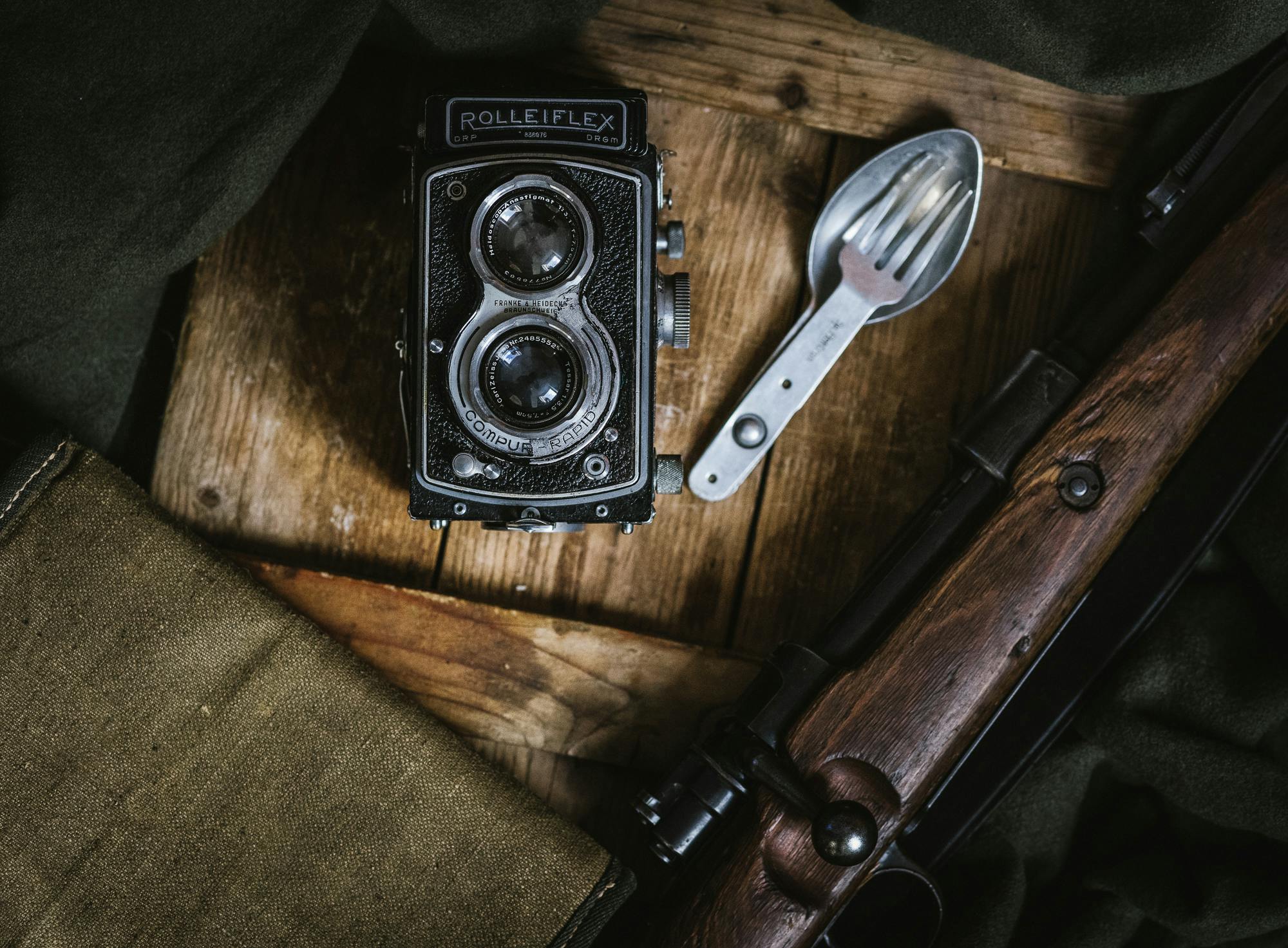 an old camera sitting on top of a wooden table, a still life, by Adam Marczyński, pexels contest winner, military weaponry, rolleiflex tlr, cutlery, vanilla