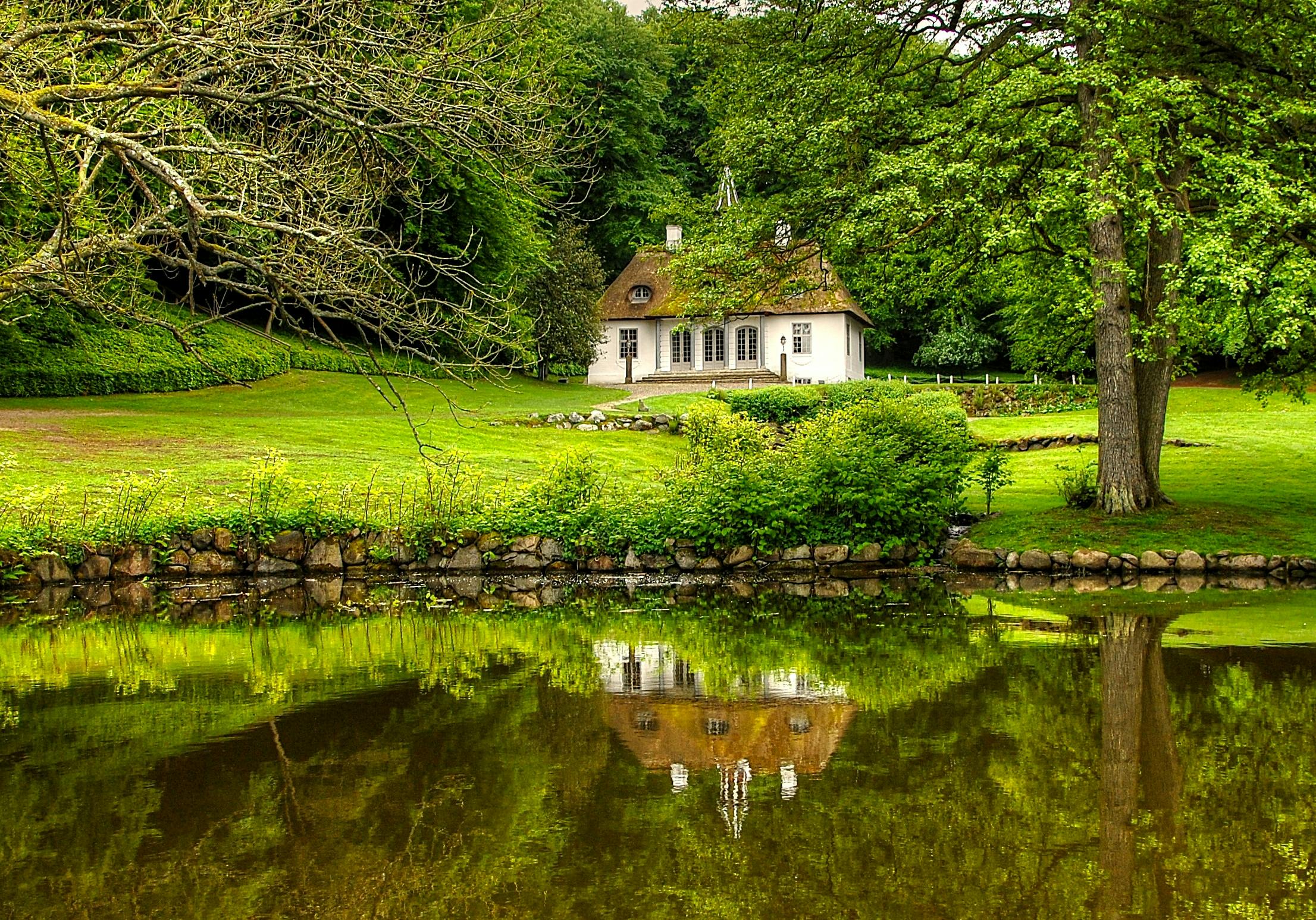 a small white house sitting on top of a lush green field, a photo, by Sebastian Spreng, pixabay contest winner, renaissance, reflections on the water, alvar aalto, woodland setting, brown