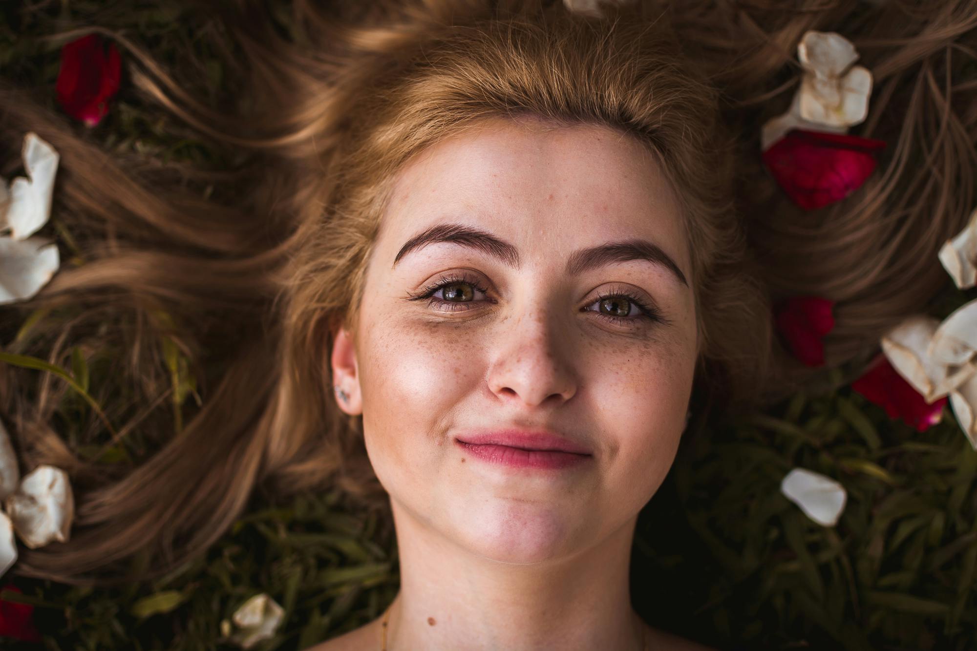 a woman laying on top of a lush green field of flowers, a character portrait, inspired by Elsa Bleda, pexels contest winner, renaissance, close-up perfect face, rose in hair, smiling down from above, color photograph portrait 4k