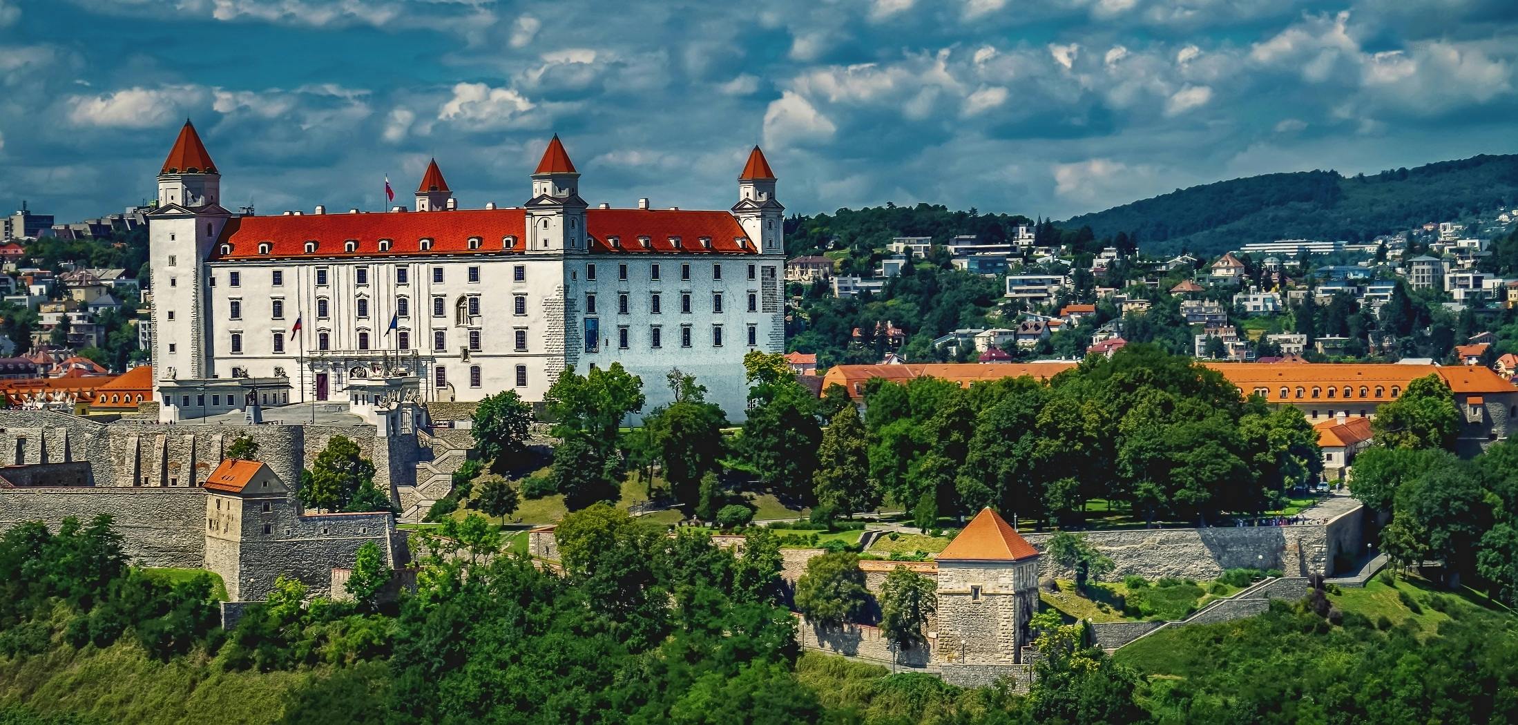 a castle sitting on top of a lush green hillside, white buildings with red roofs, janusz jurek, featured, square
