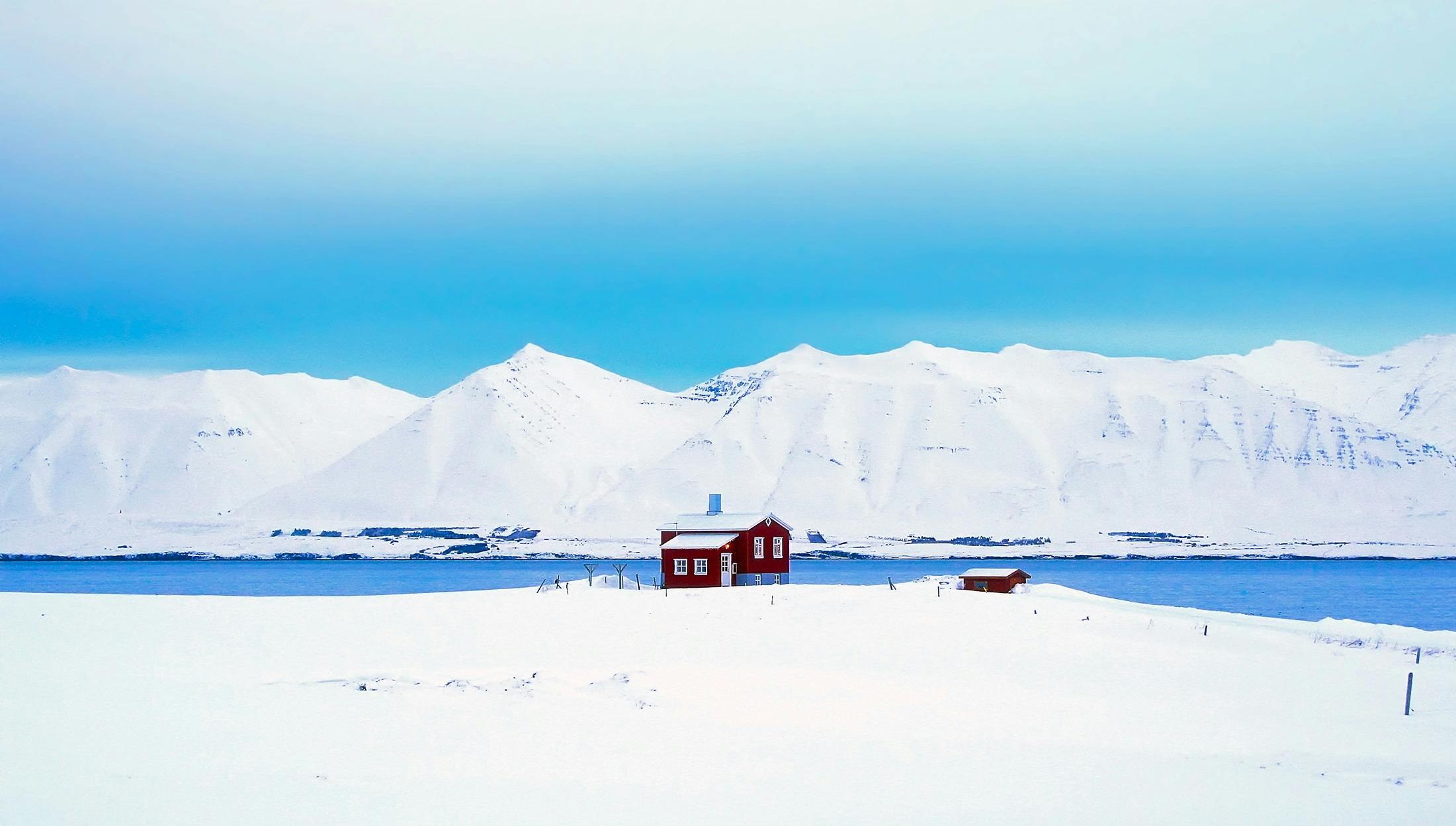 a red house sitting on top of a snow covered field, inspired by Scarlett Hooft Graafland, pexels contest winner, white and blue, in the iceland calm water, background image, mountains in a background