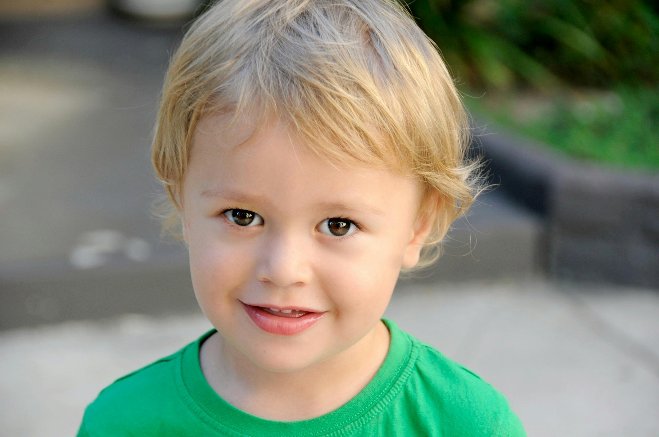 a close up of a child wearing a green shirt, blonde hair and blue eyes, small beard, photograph, young child