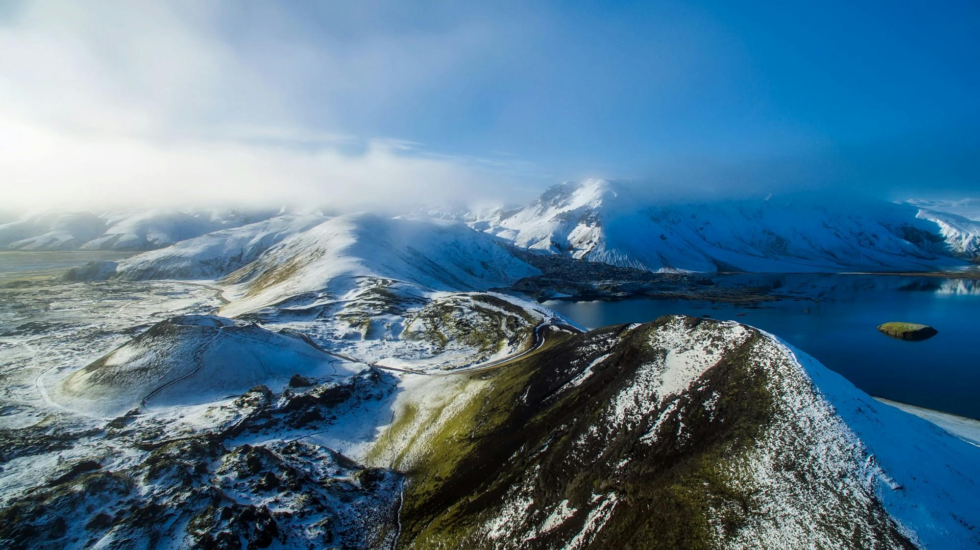 a large body of water surrounded by snow covered mountains, by Peter Churcher, pexels contest winner, hurufiyya, volcanic landscape, drone photograpghy, icewind dale, over the hills