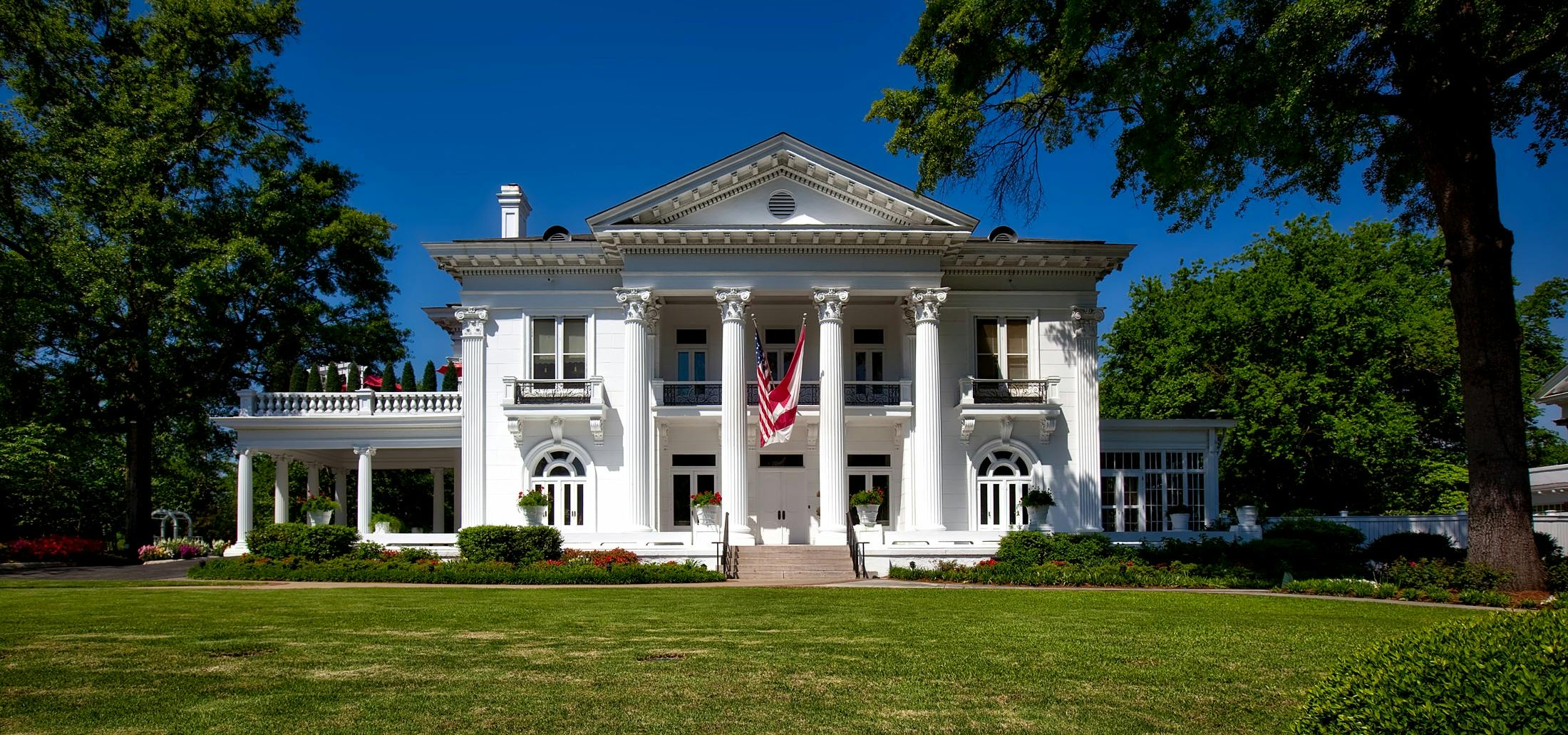 a large white house sitting on top of a lush green field, alabama, profile image, colonnade, lavishly decorated