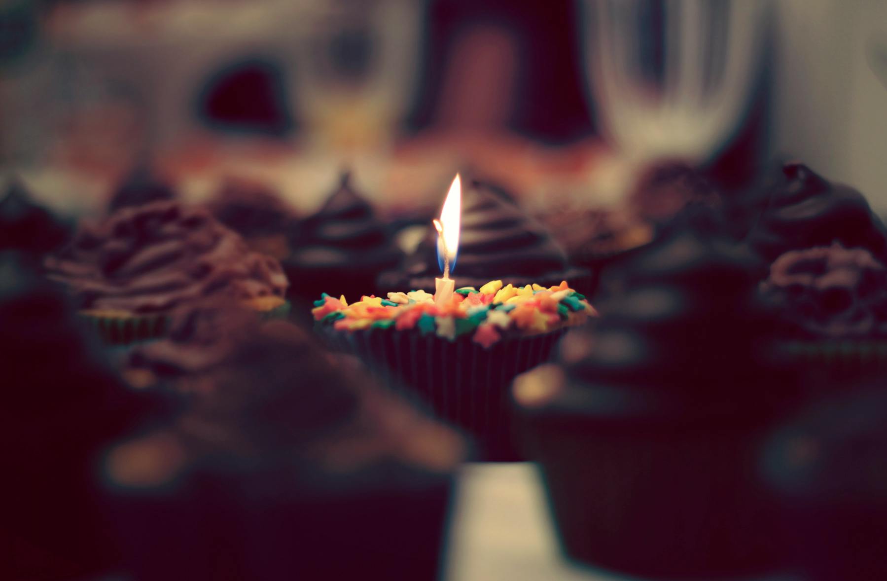a close up of a cupcake with a lit candle, a tilt shift photo, by Karl Buesgen, pexels, happening, retro stylised, black, birthday, instagram photo