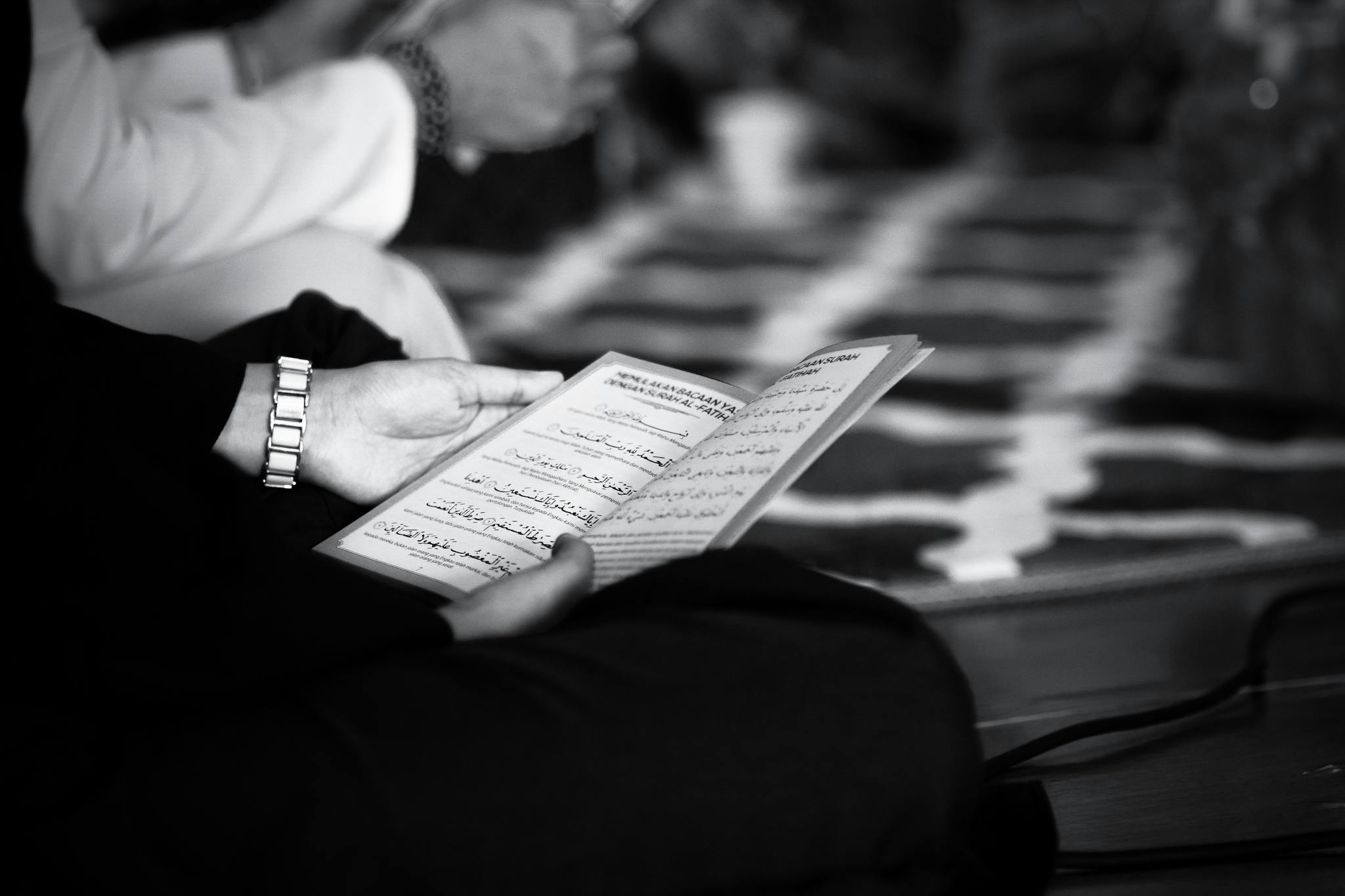 a black and white photo of a person reading a book, hurufiyya, focus on the musicians, prayer, high quality upload, uploaded
