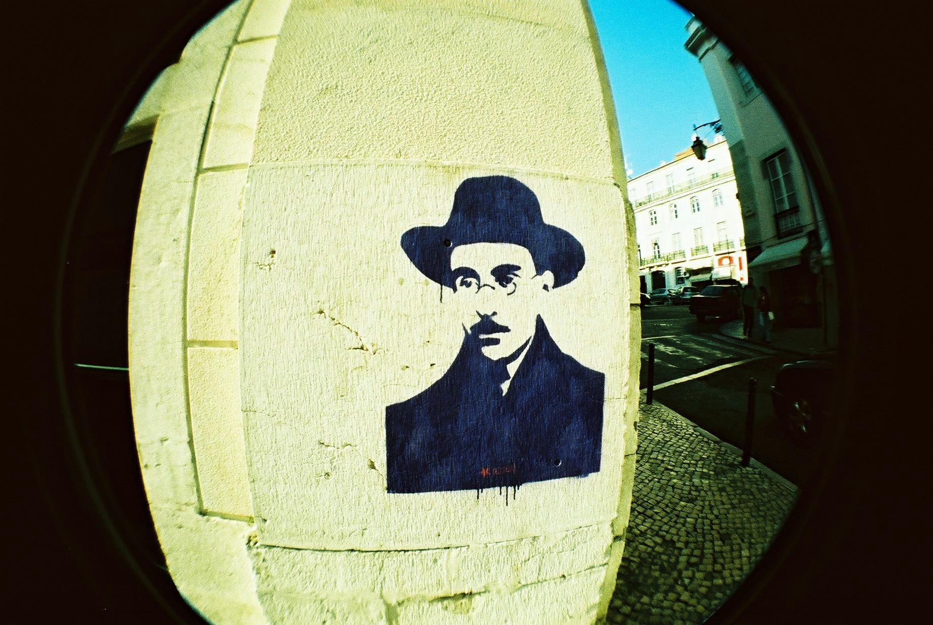 a picture of a man in a hat on a wall, a polaroid photo, inspired by René Magritte, street art, jewish young man with glasses, lisbon, fisheye photo, avatar image