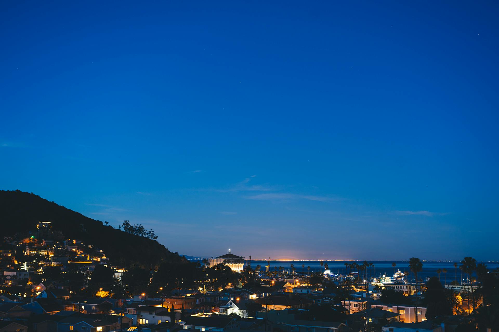 a view of a city at night from the top of a hill, by Carey Morris, unsplash, blue and clear sky, vallejo, summer evening, seaside
