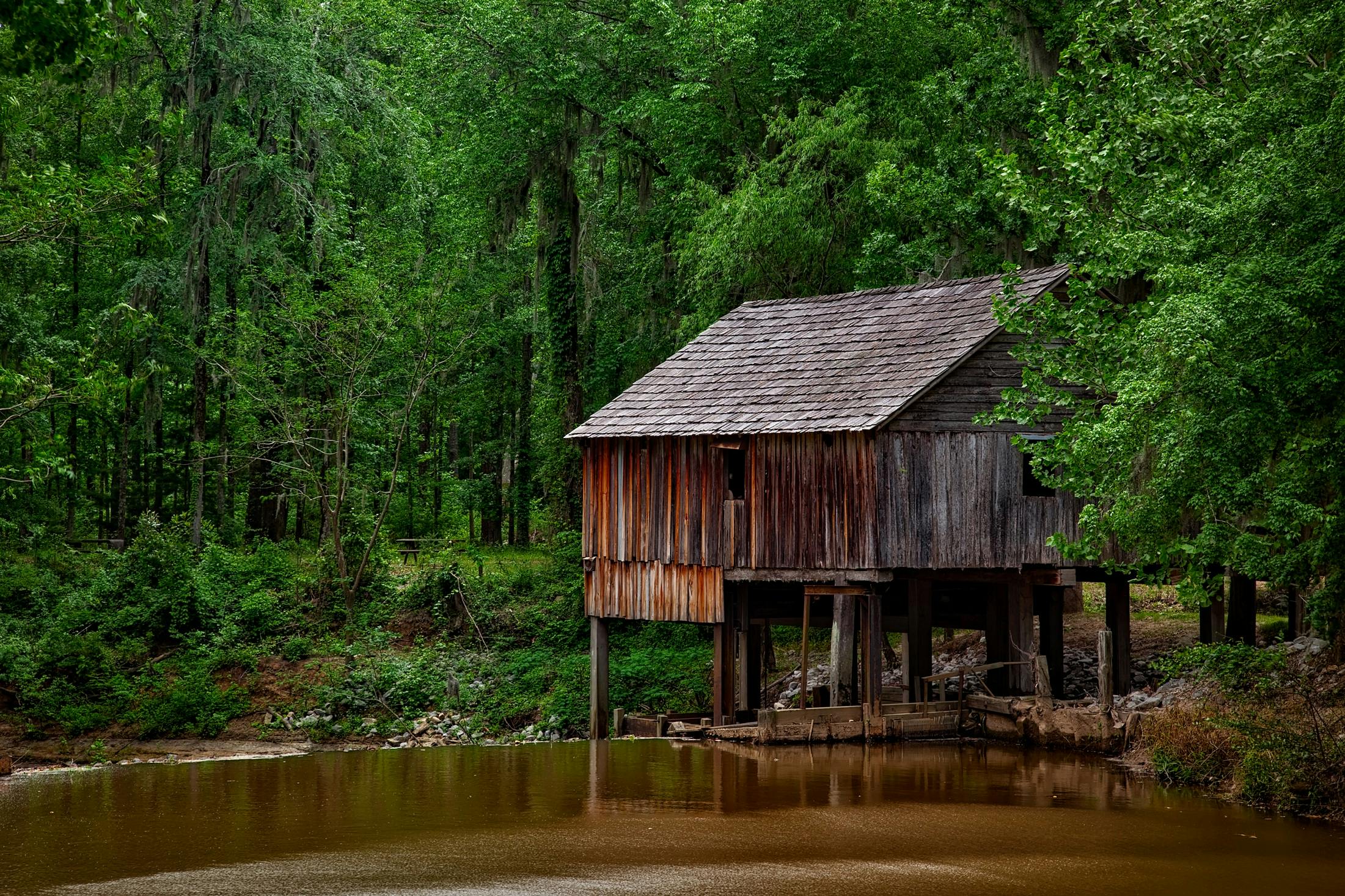 a wooden house sitting on top of a body of water, inspired by Asher Brown Durand, renaissance, backwater bayou, exterior photo, fan favorite, lush surroundings