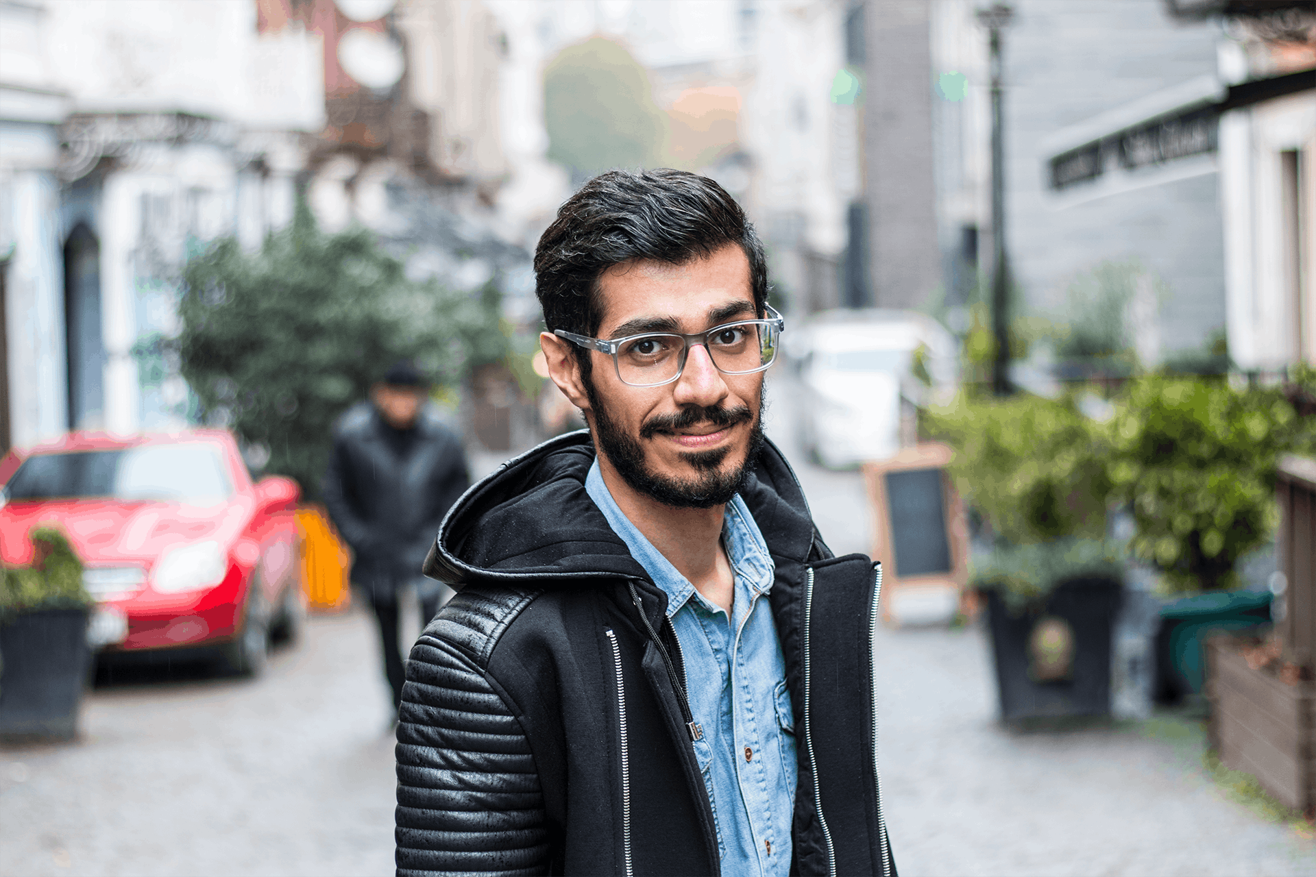 a man wearing glasses standing in the middle of a street, a picture, hurufiyya, wearing a jeans jackets, smiling and looking directly, raden saleh, profile image