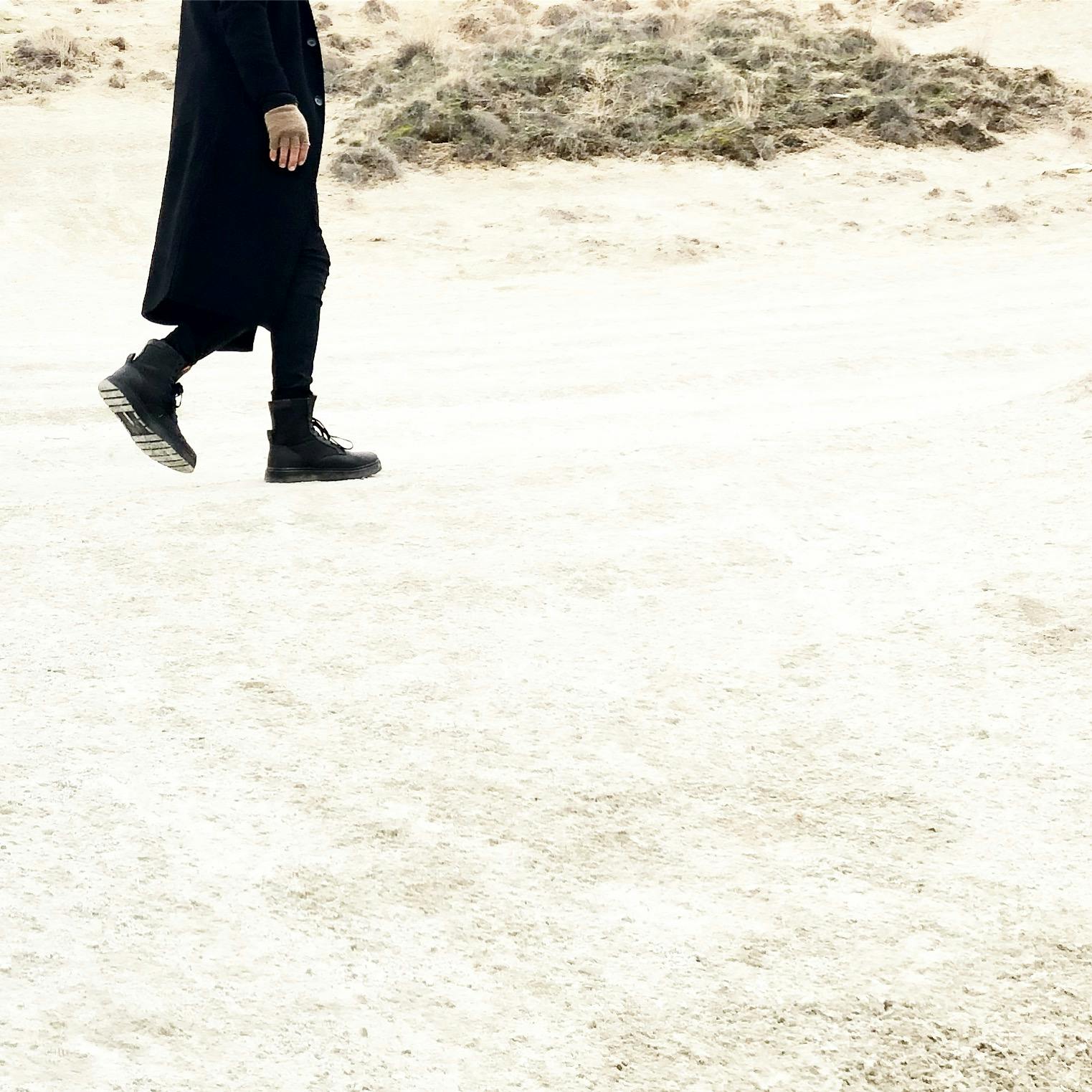 a man in black walking down a beach path