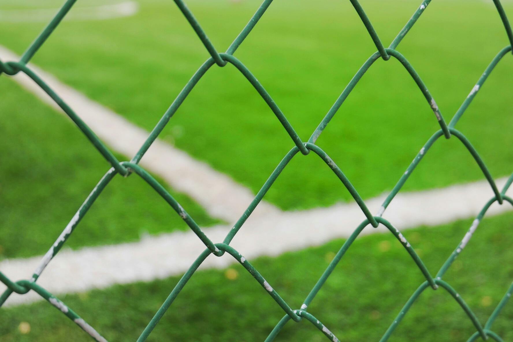 a chain link fence with baseball field in the background