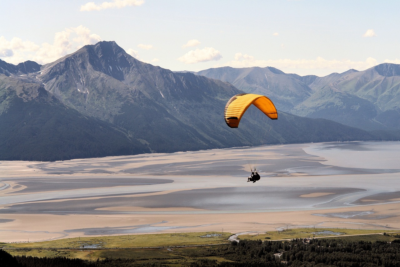 a person parasailing over a body of water with mountains in the background, a picture, by Andrei Kolkoutine, flickr, hovering above a lake in yukon, dune, slightly golden, parachutes