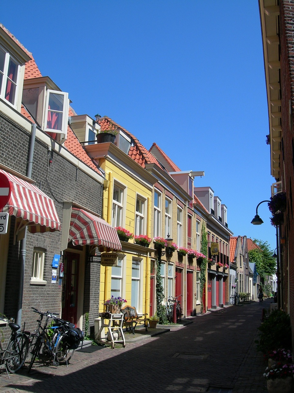 a group of bicycles parked on the side of a street, a photo, by Jan Tengnagel, flickr, de stijl, sunlight and whimsical houses, helmond, colonial era street, coastal
