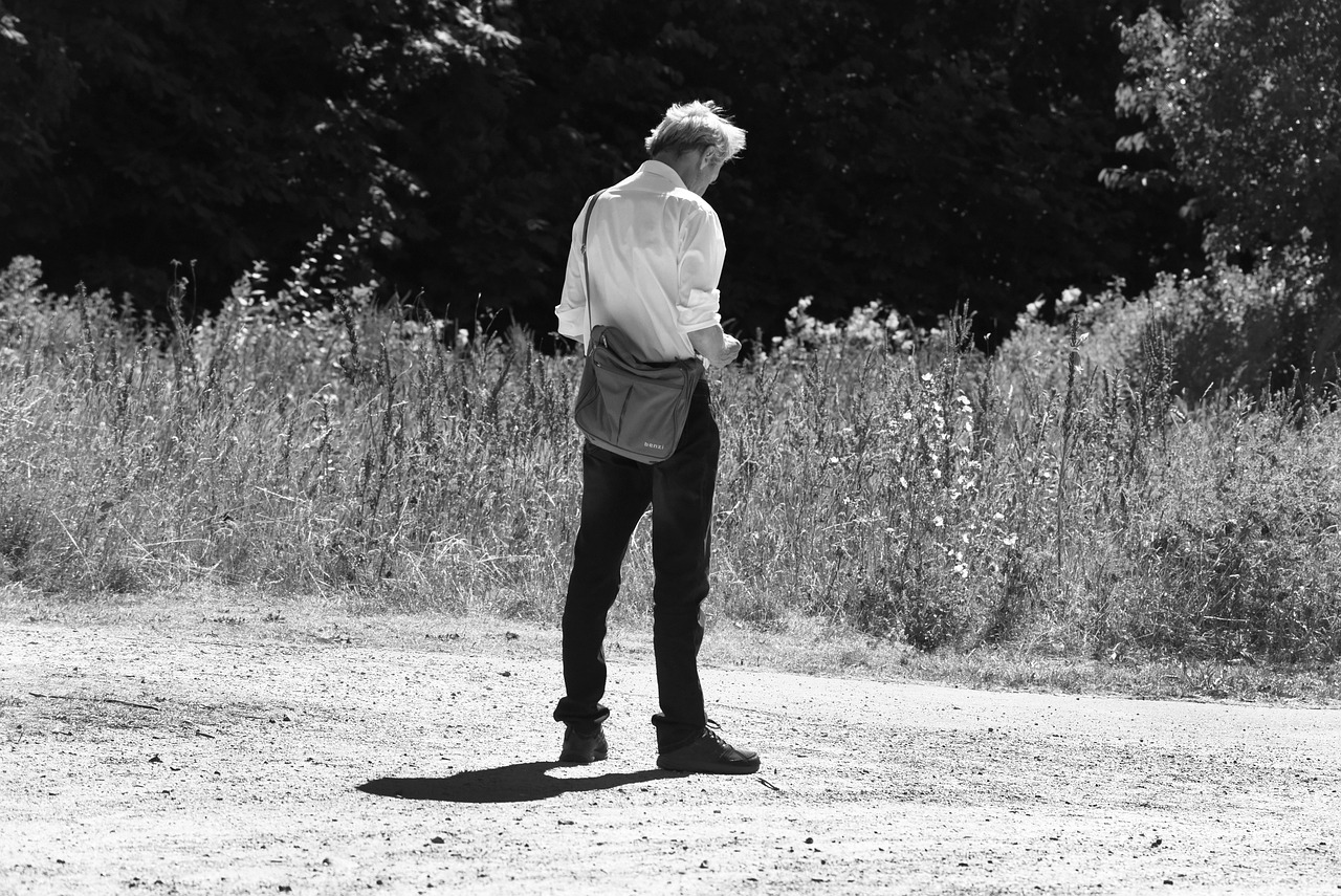 a black and white photo of a man standing on a dirt road, a black and white photo, inspired by August Sander, delicate androgynous prince, hot summer sun, bag over the waist, one man is blond