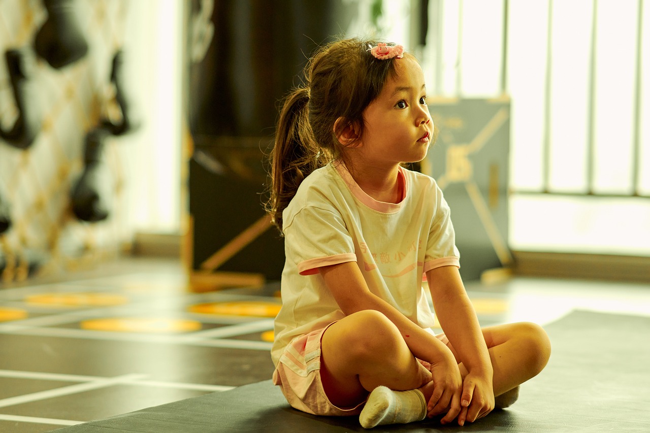 a little girl sitting on the floor with a tennis racket, pexels, realism, chun li at the gym, pensive and hopeful expression, softplay, lotus pose