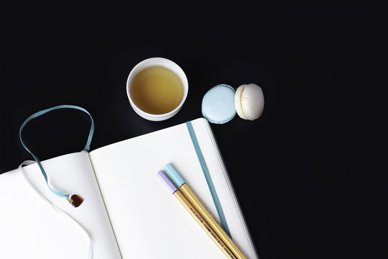 a cup of tea next to a notebook and a pair of chopsticks, minimalism, macaron, black cyan gold and aqua colors, food blog photo, taken in the night