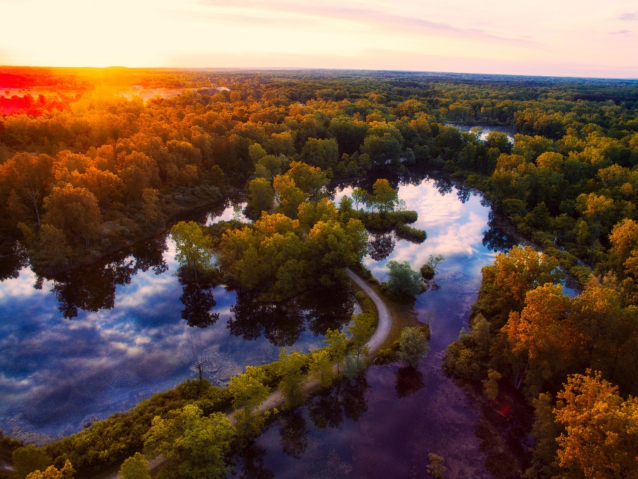 a river running through a lush green forest, by Jacob Kainen, pexels, autumn sunrise warm light, aerial view cinestill 800t 18mm, michigan, located in a swamp at sunrise