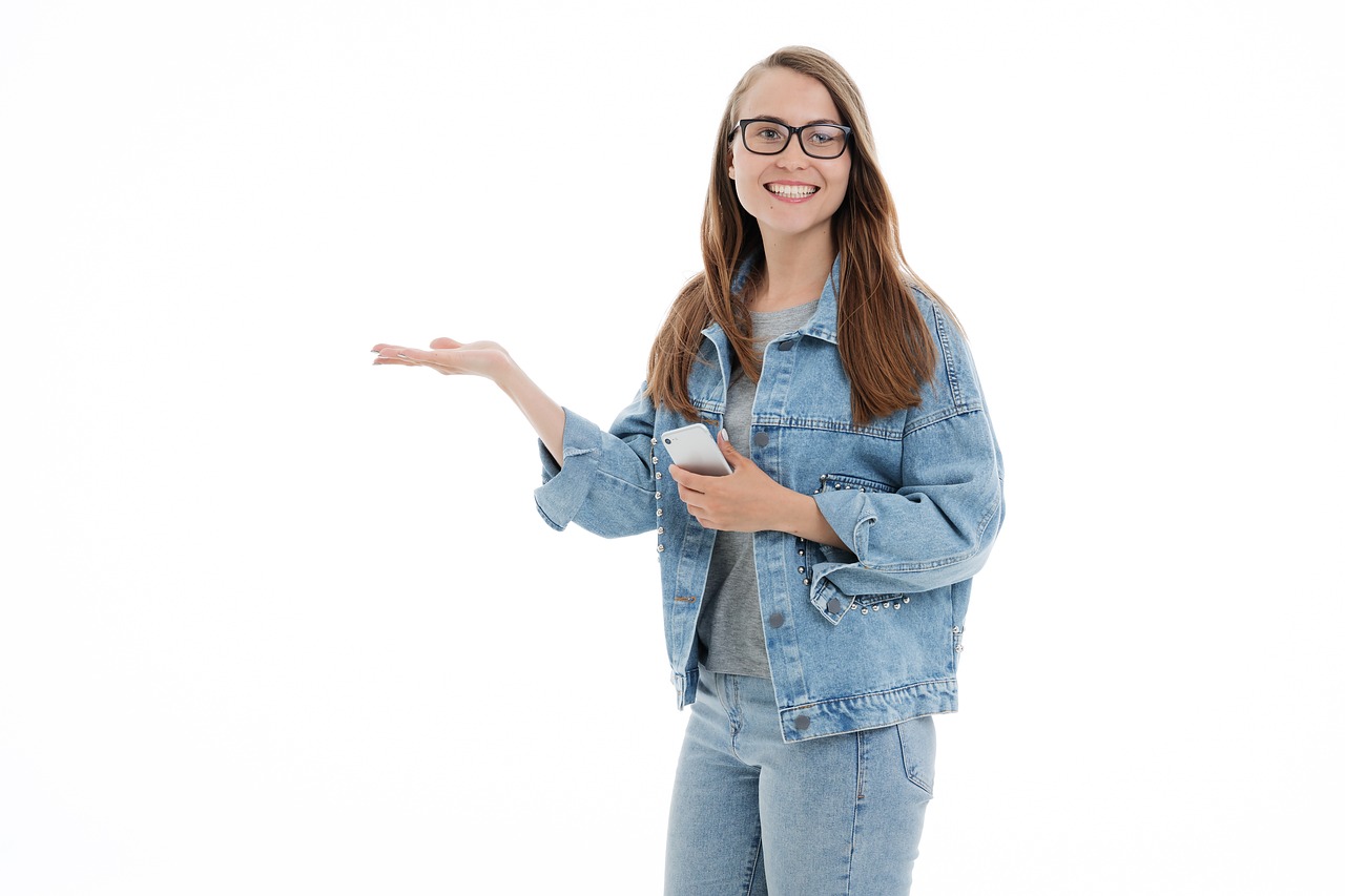 a woman in a denim jacket holding a cell phone, a picture, shutterstock, realism, waving and smiling, set against a white background, wearing small round glasses, presenting wares