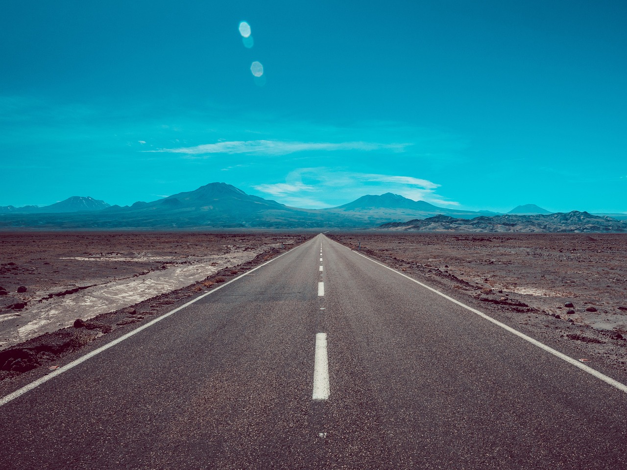 a road in the middle of a desert with mountains in the background, a picture, by Andrei Kolkoutine, shutterstock, postminimalism, clear blue sky vintage style, computer wallpaper, andes, telephoto long distance shot