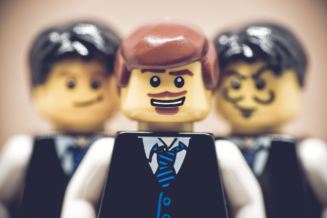 a couple of lego men standing next to each other, a tilt shift photo, wearing a vest and a tie, highly detailed photo of happy, trio, wearing a school uniform