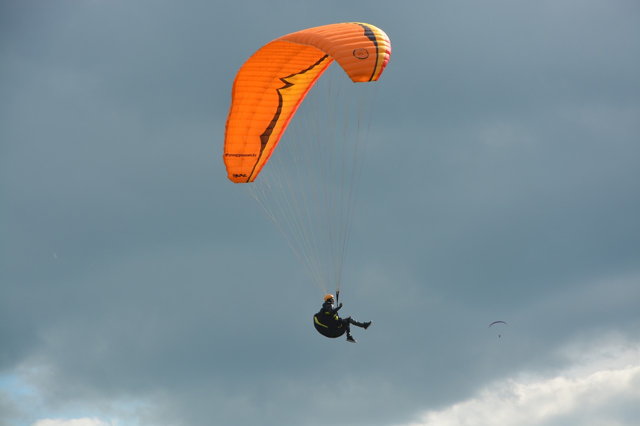 a person that is in the air with a parachute, by David Burton-Richardson, flickr, hurufiyya, vibrant but dreary orange, octane fender, nice slight overcast weather, filmed in 70mm