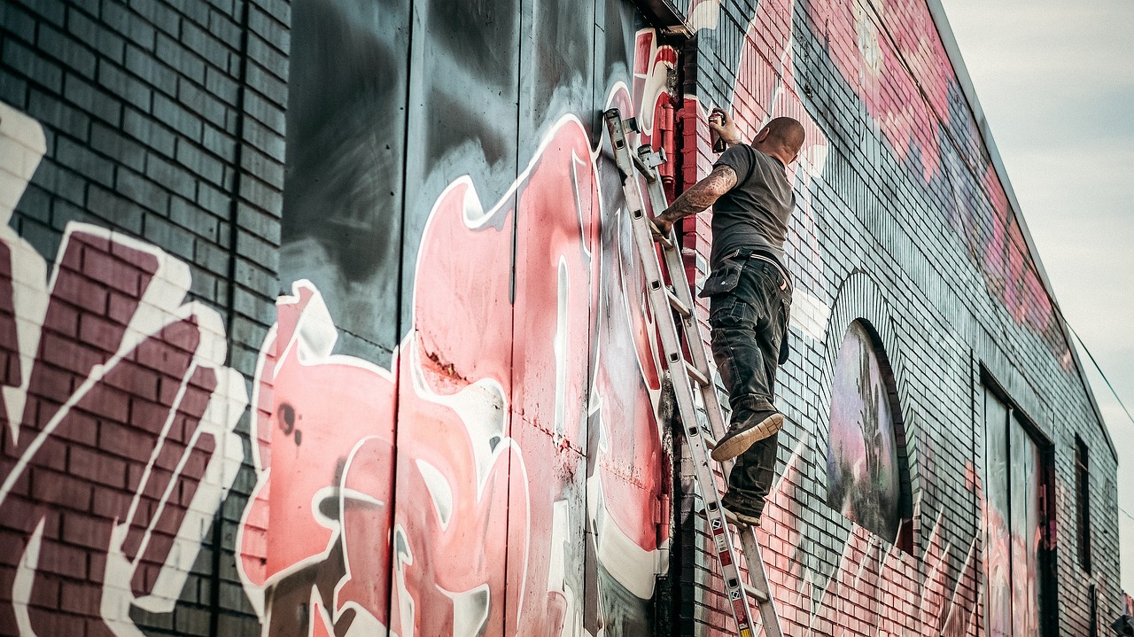 a man on a ladder painting graffiti on the side of a building, graffiti art, by Matt Stewart, pexels, it has a red and black paint, faded and dusty, old man doing hard work, parkour
