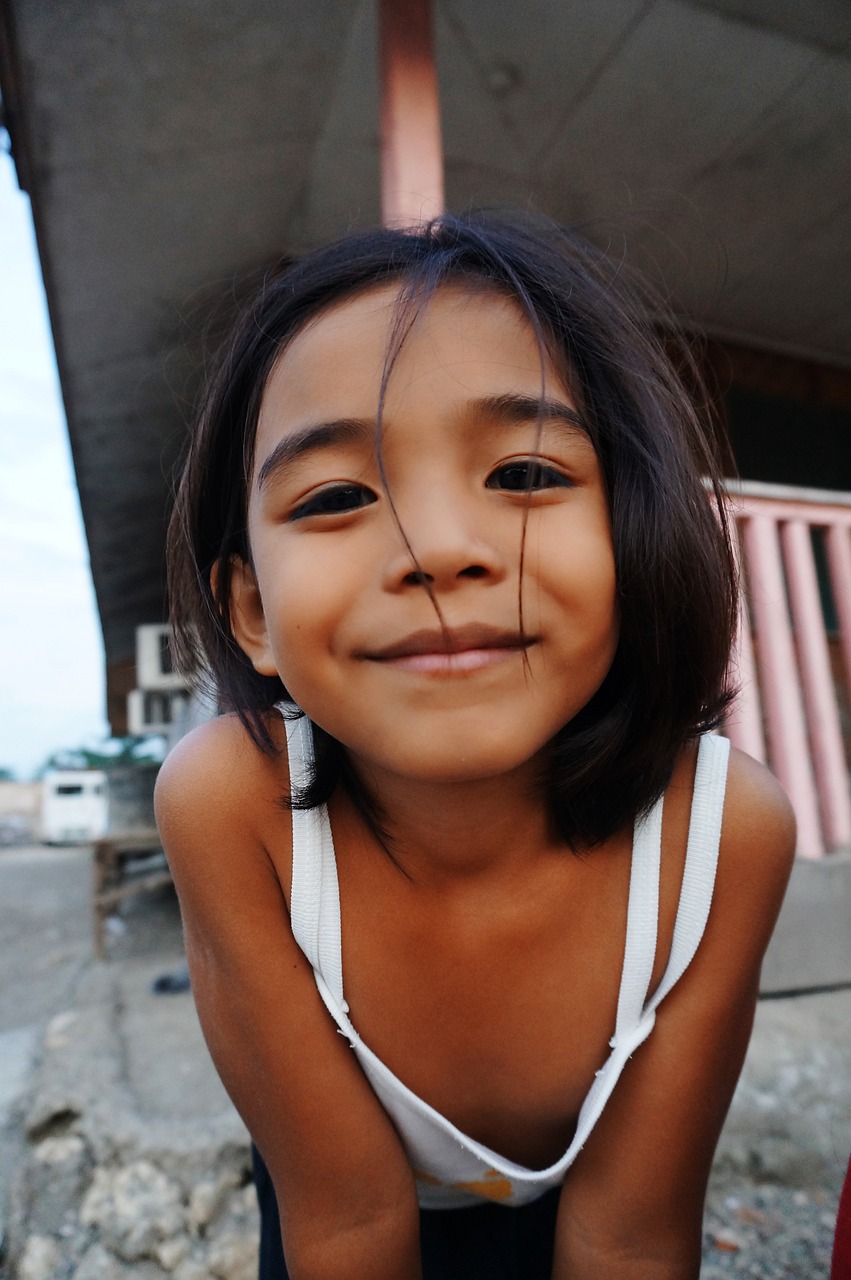 a little girl posing for a picture in front of a building, a picture, philippines, closeup of face, turning her head and smiling, bottom angle
