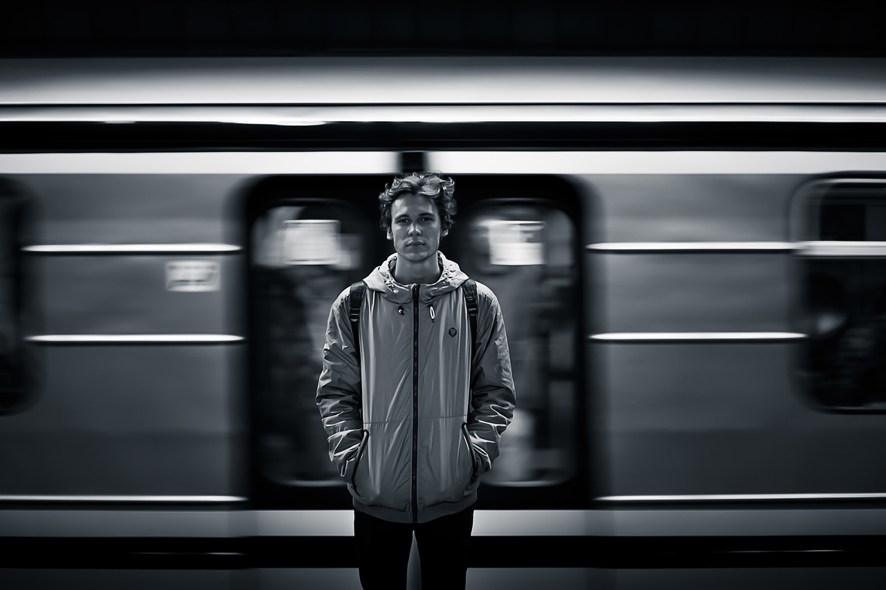 a man standing in front of a train, a black and white photo, by Matthias Weischer, male teenager, portrait. 8 k high definition, subway station, flash photo