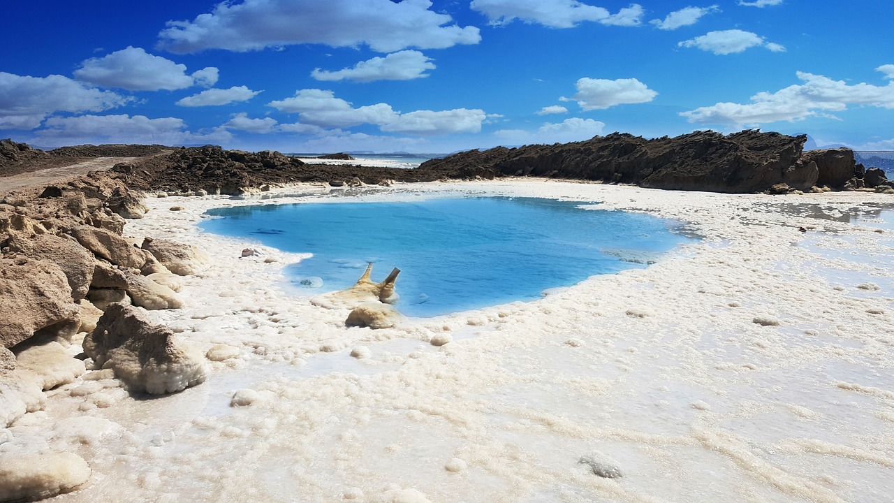 a large body of water sitting on top of a sandy beach, a photo, inspired by Scarlett Hooft Graafland, unsplash contest winner, process art, sulfur, white and blue, in a desert oasis lake, bubbling geysers