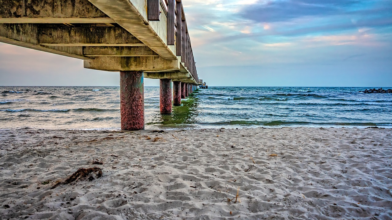 a sandy beach under a bridge on a cloudy day, a stock photo, by Ivan Grohar, shutterstock, renaissance, near a jetty, florida, details and vivid colors, concrete pillars