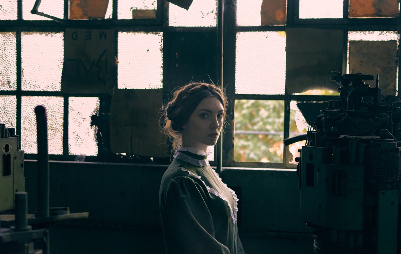 a woman standing in front of a machine in a factory, a portrait, inspired by Nikolai Ge, unsplash, art nouveau, set photo in costume, cinematographic shot, wearing victorian clothes, inspired in balthus