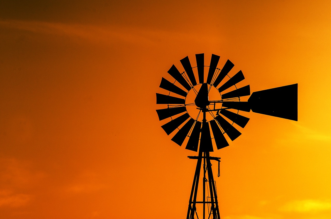 a windmill is silhouetted against an orange sky, a stock photo, precisionism, golden hour closeup photo, on wild west, shot in canon 50mm f/1.2, farming