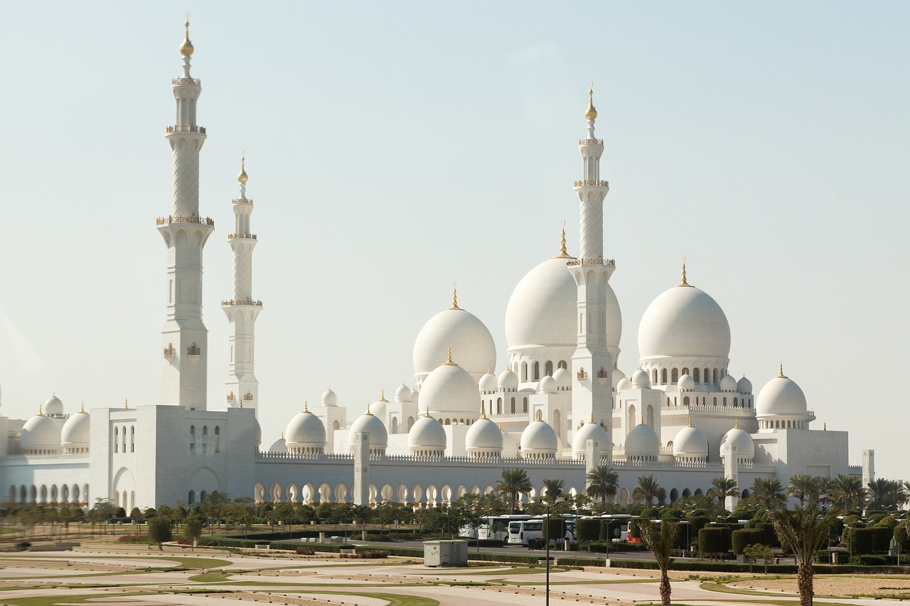 a large white building sitting on top of a lush green field, inspired by Sheikh Hamdullah, arabesque, black domes and spires, in the desert beside the gulf, massive structures, domes