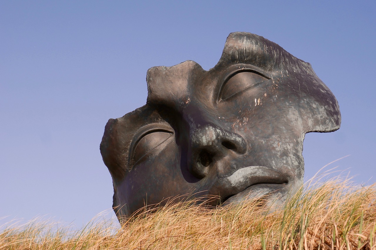 a close up of a statue of a person's face, a surrealist sculpture, by Dietmar Damerau, flickr, hillside, facing each other, on dune, reclining