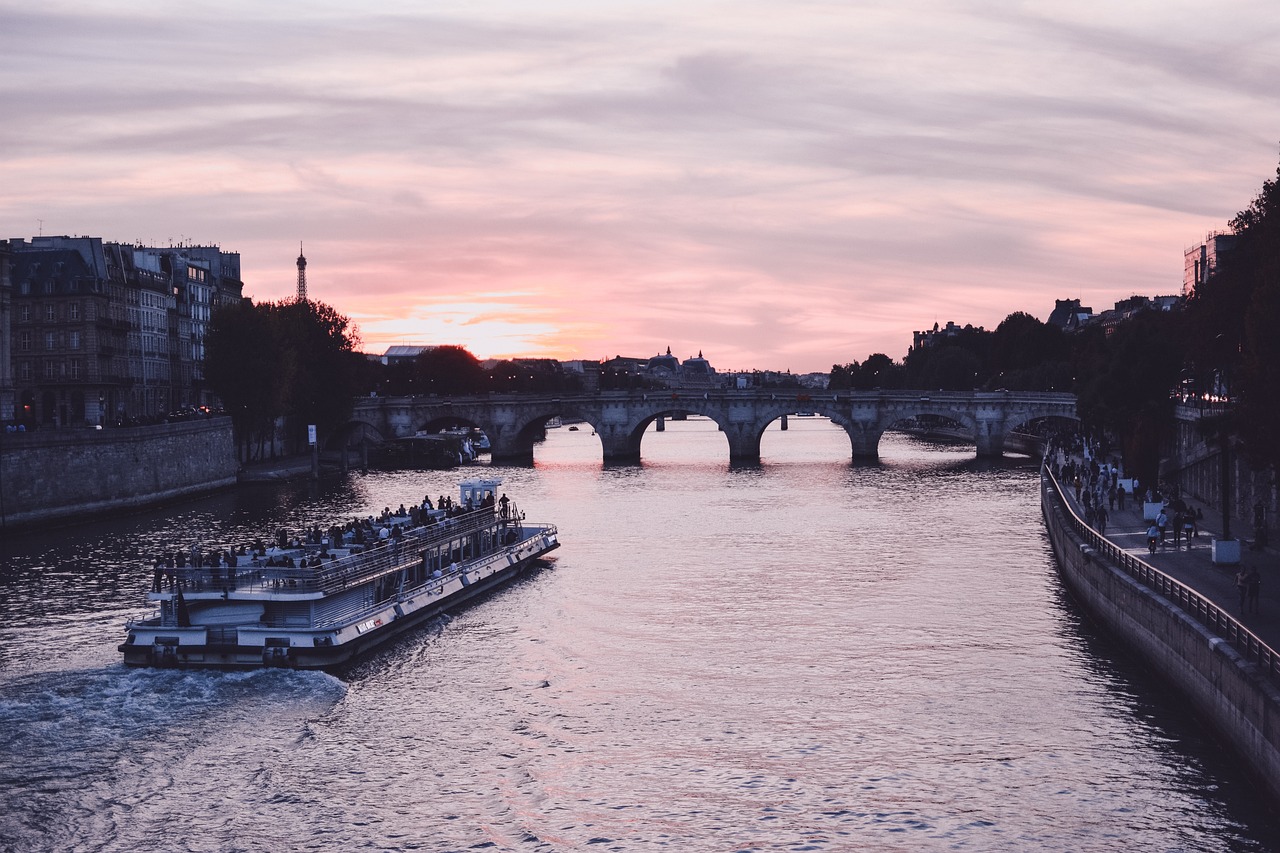 a boat traveling down a river next to a bridge, by Raphaël Collin, pexels contest winner, romanticism, pink sunset hue, paris, francois - edouard picot, side