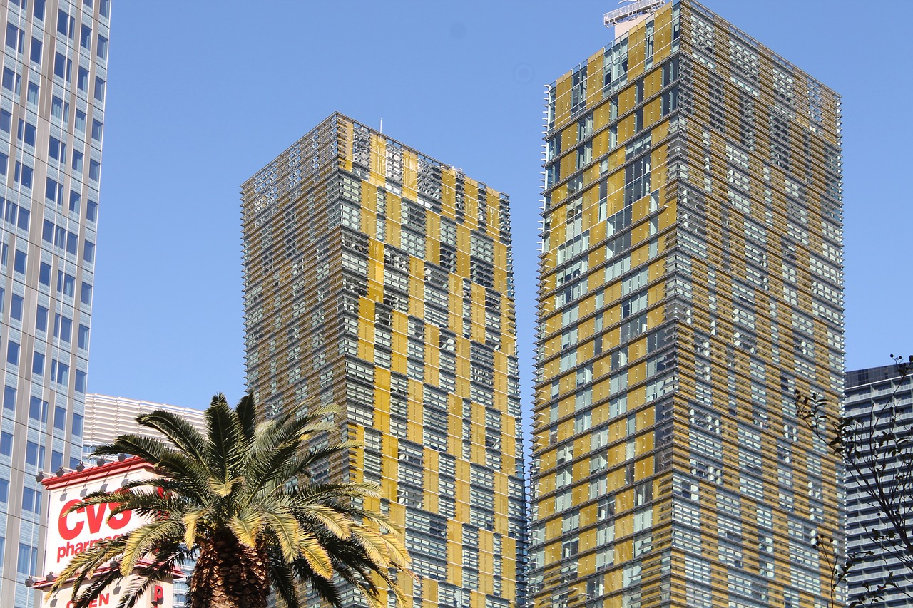 a tall building with a palm tree in front of it, inspired by Ned M. Seidler, flickr, silver and yellow color scheme, two towers, las vegas, multi layered huge architectures