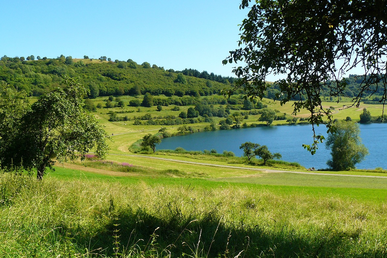 a large body of water sitting on top of a lush green hillside, by Edward Corbett, flickr, brockholes, magical sparkling lake, a wooden, golf course in background